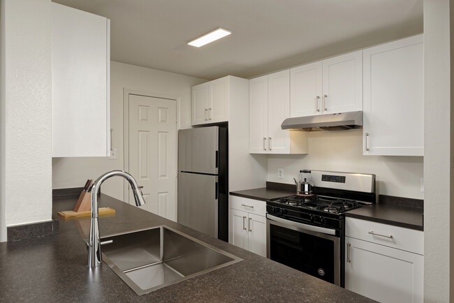 Cocina renovada del Paquete II con gabinetes blancos, encimeras de laminado gris oscuro, electrodomésticos de acero inoxidable y pisos de superficie dura - eaves Washingtonian Center