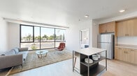 Located at 918 20th St, Unit 208 in Bakersfield, CA, this thoughtfully designed one-bedroom unit offers a clean, contemporary aesthetic across a well-utilized single floor. Light wood-plank flooring runs throughout, tying together each area with a warm, cohesive feel.

The open-concept living area is a standout feature, anchored by expansive floor-to-ceiling windows with bold black frames that flood the space with natural light and offer open views of the surrounding Bakersfield streetscape, including palm trees and the wider neighborhood. A wall-mounted mini-split system provides efficient climate control.

The kitchen is well-appointed with warm-toned wood cabinetry, light quartz countertops, a stainless steel refrigerator, dishwasher, range, and microwave. A freestanding kitchen island with open shelving doubles as a casual dining spot with bar seating.

The bedroom continues the bright, airy design language, featuring large windows that frame outdoor views, a wall-mounted mini-split unit, and direct access to a generous walk-in closet with built-in rod storage and wood flooring. The bathroom is clean and functional, offering a full tub-shower combination with chrome fixtures and a crisp white surround. The overall ambiance is modern, light-filled, and efficiently organized.