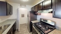 This premium single-floor residence features three bedrooms and two bathrooms within a thoughtfully designed layout. The kitchen is equipped with stainless steel appliances, including a gas range and refrigerator, complemented by rich dark cabinetry and granite-style countertops. Wood-look flooring runs through the kitchen and utility areas, adding a clean, modern touch.

The open living area is generously sized, anchored by a granite-topped breakfast bar that connects seamlessly to the kitchen. A large window fills the space with natural light and offers views of the surrounding greenery. The carpeted living area flows directly into the hallway leading to the bedrooms.

Each bedroom features plush carpet flooring and a dedicated closet for ample storage. One bedroom enjoys a bright window with outdoor views, while the primary bedroom provides direct access to an en-suite bathroom. Both bathrooms are well-appointed with granite vanity tops, dark cabinetry, tiled shower-tub combos, and wood-look flooring.

A utility closet with an electrical panel is conveniently located off the kitchen. Throughout the home, neutral walls, consistent finishes, and a clean, open feel create a comfortable and functional living environment suited for everyday living.