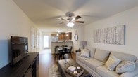 This two-floor residence offers a thoughtfully designed open-concept layout that connects the primary living areas into one cohesive space. The living room is warm and inviting, anchored by rich hardwood-style flooring and a ceiling fan with integrated lighting that ensures year-round comfort. A comfortable seating area flows naturally toward the dining space, which accommodates a full dining table and chairs, making it ideal for both everyday meals and entertaining guests. The kitchen features warm wood cabinetry, stainless steel appliances including a refrigerator, and a breakfast bar that provides additional seating and counter space. Pendant lighting above the bar adds a stylish touch, while natural light pours in through a rear-facing window and door, brightening the entire open living area. Neutral wall tones throughout create a clean and versatile backdrop that complements a variety of décor styles. A closet and entry door are visible near the front of the main floor, providing practical storage and easy access. The space extends across two floors, offering additional room and flexibility for various living arrangements. Overall, the home strikes a balance between functional design and comfortable, everyday livability.