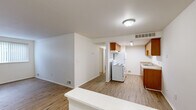 This 2-bedroom, 1-bathroom single-story unit offers a well-organized layout designed for comfortable everyday living. The combined kitchen and living area forms the heart of the home, featuring warm wood-look flooring that extends throughout the common spaces. The kitchen is equipped with warm-toned wooden cabinetry lining both walls, a white electric range, a refrigerator, and a single-basin sink with ample counter space — providing a fully functional galley-style setup. The adjoining living area is bright and open, bathed in natural light from a large window fitted with vertical blinds.

The primary bedroom features the same wood-look flooring and offers a generously proportioned layout with good natural light. The second bedroom is carpeted and similarly well-lit, with a window overlooking greenery outside. Both bedrooms are served by two dedicated closets, providing practical storage throughout the unit.

The bathroom is clean and straightforward, featuring a full-size soaking tub with a tiled shower surround, a toilet, and classic white fixtures. Throughout the unit, white walls and neutral finishes create a clean, understated aesthetic. The floor plan flows efficiently, with each room clearly defined yet easily accessible, making this a functional and comfortable living space.