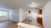 This 2-bedroom, 1-bathroom single-story unit offers a well-organized layout designed for comfortable everyday living. The combined kitchen and living area forms the heart of the home, featuring warm wood-look flooring that extends throughout the common spaces. The kitchen is equipped with warm-toned wooden cabinetry lining both walls, a white electric range, a refrigerator, and a single-basin sink with ample counter space — providing a fully functional galley-style setup. The adjoining living area is bright and open, bathed in natural light from a large window fitted with vertical blinds.

The primary bedroom features the same wood-look flooring and offers a generously proportioned layout with good natural light. The second bedroom is carpeted and similarly well-lit, with a window overlooking greenery outside. Both bedrooms are served by two dedicated closets, providing practical storage throughout the unit.

The bathroom is clean and straightforward, featuring a full-size soaking tub with a tiled shower surround, a toilet, and classic white fixtures. Throughout the unit, white walls and neutral finishes create a clean, understated aesthetic. The floor plan flows efficiently, with each room clearly defined yet easily accessible, making this a functional and comfortable living space.