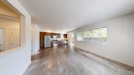 Located in Kenmore, WA, this one-bedroom, one-bathroom unit offers a thoughtfully designed layout across a single floor. The open-concept kitchen and living area is a standout feature, showcasing polished concrete floors that lend an urban, contemporary feel throughout the main living space. The kitchen is well-appointed with rich wood cabinetry, stainless steel appliances including a refrigerator, electric range, microwave, and dishwasher, complemented by light countertops and a single-basin sink. Large windows and a sliding glass door flood the living area with natural light and provide views of the surrounding mature tree canopy. A pass-through window connects the kitchen to an adjacent area, adding an architectural detail that enhances the open feel. The bedroom is carpeted for comfort and features its own dedicated closet with built-in shelving, offering practical storage. An additional window in the bedroom brings in natural light. The bathroom includes a full tub-shower combination, a vanity with wood cabinetry, and tile-style flooring. Outside, a gated entry with brick detailing and landscaped greenery provides a welcoming approach to the unit.