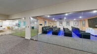 The amenities floor at The Residence at 1000 Elm in Manchester, New Hampshire, delivers a generously sized, thoughtfully designed space dedicated entirely to resident recreation and community. The floor is anchored by a vibrant lobby lounge that sets the tone with bold teal accent walls, wood-look flooring, and eclectic, colorful furniture including sculptural orange and pink seating, a gold disc coffee table, and a tufted yellow bench — creating an energetic yet welcoming arrival experience.

The fully equipped fitness center is enclosed in sleek floor-to-ceiling glass walls, offering a well-stocked gym with cardio equipment, free weights, medicine balls, stability balls, and open exercise space — all illuminated by recessed lighting with subtle blue accent lighting at the base.

Adjacent to the gym, a private screening room features rows of plush leather recliner seating, framed movie posters, and ambient blue lighting, accessible through a glass-paneled sliding door for a true theater experience.

The communal kitchen is a standout feature, showcasing white shaker cabinetry, quartz countertops, stainless steel appliances, a large center island with gold-toned pendant lighting, and bold teal accent walls. Flexible open corridors adorned with local photography complete the floor, providing multifunctional gathering and event space throughout.
