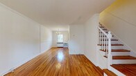 Located at Knickerbocker Road in Dumont, NJ, this two-story home offers a well-organized layout spread across two floors. The main level features a spacious living and dining area highlighted by warm, polished hardwood floors that run throughout, crisp white walls, crown molding, and a classic chandelier that adds a touch of elegance. Natural light flows in through multiple windows, creating a bright and welcoming atmosphere. A staircase with white balusters and wood treads connects the two floors seamlessly.

The kitchen is equipped with stainless steel appliances, including a full-size refrigerator and range, set against light-toned flooring. The full bathroom is clean and modern, featuring white subway tile surrounding a soaking tub and shower, marble-look tile flooring, a sleek vanity with contemporary fixtures, and a window for natural ventilation.

Upstairs, two bedrooms continue the hardwood flooring theme. Each room benefits from natural light through double-hung windows with garden views, wall-mounted air conditioning units, and radiator heating. The spacious primary bedroom offers a comfortable retreat, while the second bedroom provides flexible use as a guest room or home office. The home's neutral palette and consistent finishes give it a cohesive, move-in-ready appeal.