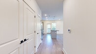 This thoughtfully designed single-story residence offers a seamless blend of modern finishes and functional layout. The open-concept kitchen and living area serves as the heart of the home, featuring a central island with a dark granite countertop and built-in sink, white shaker-style cabinetry with brushed gold hardware, a classic subway tile backsplash, and a full suite of stainless steel appliances. Pendant lighting above the island and recessed ceiling lights provide both task and ambient illumination, while a large window invites natural light and outdoor views into the space. Light wood-tone luxury vinyl flooring runs throughout the main living areas, lending a clean and cohesive aesthetic. A welcoming hallway with panel-style doors and black hardware connects the living areas to the private quarters. The bedroom is carpeted for comfort, includes a ceiling fan, a walk-in closet, and a window with views of greenery. The bathroom is well-appointed with a full soaking tub and shower combo, a white vanity with dark granite countertops, and a framed mirror. Throughout, the unit maintains a crisp, neutral palette with white walls and bright recessed lighting, creating a fresh and move-in-ready atmosphere.