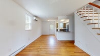 This three-floor home is designed with a clean, functional aesthetic throughout. The main living level features warm hardwood flooring that extends through the open living area and into the adjacent rooms. Natural light enters through multiple windows fitted with blinds, creating a bright and airy atmosphere. A wall-mounted mini-split unit provides climate control, complemented by baseboard heating along the perimeter walls. A staircase with a wood railing connects the levels, adding a classic structural element to the main floor.

The kitchen is well-appointed with gray shaker-style cabinetry, dark granite countertops, and a full suite of stainless steel appliances including a refrigerator, range, microwave, and dishwasher. A pass-through opening connects the kitchen to the living area, enhancing the open flow of the space. Light tile flooring grounds the kitchen and contrasts with the hardwood in adjacent rooms.

The bedrooms continue the hardwood flooring and white-walled palette, each benefiting from natural light through well-placed windows. The bathroom features classic white subway tile surrounding a soaking tub, with a window providing ventilation and natural light. The basement level offers unfinished utility space with painted concrete floors, concrete block walls, and exposed mechanical systems.