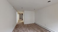 This single-floor unit offers a practical, well-organized layout comprising several rooms connected by a central hallway. The living and bedroom areas are finished with neutral-toned wall-to-wall carpeting, providing a comfortable feel throughout. Recessed lighting illuminates the main spaces, while baseboard heaters run along the walls, ensuring efficient climate control across multiple rooms.

One of the bedrooms features a wide double closet with paneled doors, offering generous storage. Another room benefits from a row of windows fitted with white blinds, allowing natural light to filter in. A private entry area includes an exterior door alongside a window, brightening the entryway.

The kitchen is well-appointed with rich, dark cherry-toned cabinetry extending to the ceiling, dark granite-style countertops, and dark tile flooring. White appliances, including a range, over-the-range microwave, and dishwasher, complete the functional cooking space.

Two bathrooms serve the unit. The full bathroom features a tiled tub-and-shower combination with a subtle mosaic accent border and light tile flooring. The second bathroom includes a dark-toned vanity with a countertop sink and light tile flooring. Throughout, the unit maintains a clean, neutral palette with white walls and trim.