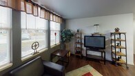 This single-floor, one-bedroom, one-bathroom unit is thoughtfully designed to maximize functionality across its well-organized layout. The living room serves as a welcoming centerpiece, featuring dark hardwood-style flooring, warm-toned accent walls, and a bank of large windows dressed with valances and blinds that invite generous natural light and offer views of the surrounding area. The space comfortably accommodates a seating arrangement and entertainment setup.

The kitchen is efficiently laid out in a U-shaped configuration, showcasing dark laminate cabinetry with sleek hardware, granite-style countertops, and a full suite of stainless steel appliances including a range, microwave, dishwasher, and refrigerator. A overhead light fixture brightens the workspace, and a breakfast bar provides additional prep or dining space.

The bedroom offers a calm, neutral environment with plush carpeting, recessed lighting, and a mirrored sliding-door closet providing ample storage. The bathroom features dark granite-topped vanity cabinetry and wood-style flooring. An in-unit washer and dryer add notable everyday convenience, completing this practical and cohesive living space.