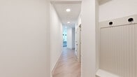 This well-appointed single-story home offers two bedrooms and two bathrooms within a thoughtfully designed, modern layout. Light wood-tone flooring runs throughout, creating a cohesive and airy feel across every room.

The kitchen serves as the heart of the home, showcasing a large center island with a white quartz countertop, a deep single-basin sink with a matte black faucet, and striking pendant lighting overhead. Gray shaker-style cabinetry, a herringbone tile backsplash, and stainless steel appliances — including a French door refrigerator and gas range — complete the space. A built-in desk area with open shelving adds a practical touch.

The hallways are bright and clean with recessed lighting, guiding residents to the private quarters. The primary bedroom is generously proportioned, featuring dual windows that invite natural light and an outdoor view, complemented by a ceiling fan. A dedicated walk-in closet offers ample organized storage with built-in shelving and dual clothing rods.

The bathrooms are finished with crisp white cabinetry, quartz countertops, matte black hardware, and a marble-style tiled tub surround. A dedicated laundry room houses a full-size washer and dryer with overhead shelving for added convenience. The second bedroom is equally bright and well-sized, with easy access to the main living areas.