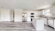 Located at 3 Ridgefield Rd in Hamburg, NJ, this single-floor home offers a thoughtfully designed layout with modern finishes throughout. The open-concept kitchen is a standout feature, showcasing crisp white shaker cabinetry, granite countertops with subtle veining, a classic subway tile backsplash, and a central island that provides additional prep and seating space. Stainless steel appliances — including a gas range, over-the-range microwave, French door refrigerator, and dishwasher — complete the culinary space, which is brightened by natural light from a window overlooking the surroundings. Consistent grey-toned luxury vinyl plank flooring flows seamlessly from the kitchen through the spacious living area, which features crown molding and multiple windows that invite abundant natural light. A wide hallway connects the living spaces to the private quarters, which include a walk-in closet with a full-length hanging rod. The bathrooms are finished with large-format grey tile, a soaking tub with tiled surround, and white vanities topped with granite counters. The overall aesthetic is clean, neutral, and move-in ready, offering a modern yet comfortable atmosphere throughout.