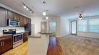 Located at 101 Integra Village Trail in Sanford, Florida, this single-story residence offers a thoughtfully designed open-concept layout with modern finishes throughout. The kitchen serves as a focal point of the main living area, showcasing rich dark-stained cabinetry, granite countertops, a subway tile backsplash, and a full suite of stainless steel appliances including a range, built-in microwave, and refrigerator. A large central island with a built-in sink and breakfast bar overhang provides additional workspace and casual dining. Pendant lights and a track lighting system illuminate the kitchen, which flows seamlessly onto warm hardwood-style flooring extending into the open living area. The living room is carpeted, bright, and accessible via a glass-paneled exterior door that invites natural light. Bedrooms are carpeted and well-lit by multiple windows with blinds, and ceiling fans are featured in the main rooms. A generously sized walk-in closet with wire shelving offers ample storage. The bathrooms feature wood-toned vanities, white countertops, large framed mirrors, and tile-surround tub-shower combinations with hardwood-style flooring. The overall ambiance is clean, contemporary, and move-in ready.