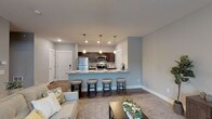 This single-floor residence offers a thoughtfully designed open-concept layout that seamlessly connects the living and kitchen areas. The kitchen is a standout feature, equipped with rich dark-wood cabinetry, stainless steel appliances including a refrigerator, microwave, and range, and expansive granite countertops. A large peninsula with seating for several barstools serves as both a casual dining space and a natural divider between the kitchen and living area. Pendant lighting above the peninsula adds a refined touch, while recessed lighting brightens the entire kitchen.

The living area is carpeted and bathed in natural light from a sliding glass door, which also provides outdoor access. A ceiling fan overhead adds comfort, and the neutral gray walls create a calm, cohesive ambiance throughout the space.

The bedroom is generously sized with plush carpeting, a ceiling fan, and a well-organized closet with bifold doors offering ample storage. The bathroom features dark-wood vanity cabinetry with granite countertops, a tub-shower combination, and wood-look flooring. A practical stacked washer and dryer unit is conveniently integrated within the bathroom space. Throughout the residence, consistent use of neutral tones, quality finishes, and functional design create a comfortable and modern living environment.