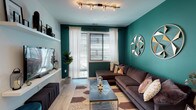 This single-floor residence makes a bold design statement through its thoughtful use of color and contemporary finishes throughout. The living area serves as the heart of the space, distinguished by a striking deep teal accent wall adorned with geometric metallic wall art. Light hardwood flooring runs underfoot, while sheer white curtains frame the windows to allow natural light to filter softly into the room. Floating white shelves along the media wall provide display space above a mounted flat-screen TV, with a teal velvet accent stool and additional seating adding personality to the layout. The kitchen is open and well-appointed, featuring dark wood cabinetry, stainless steel appliances, a mosaic tile backsplash, and a large granite-topped island with bar seating — ideal for casual dining or entertaining. Track lighting illuminates the workspace from above. The bedroom offers a warm, intimate atmosphere anchored by a rich golden-yellow accent wall and a plank-style headboard. A window with blinds and soft draping provides natural light and privacy. The bathroom is clean and modern, finished in neutral gray tones with floor-to-ceiling white tile in the tub-shower combination enclosed by sliding glass doors. Every room reflects a cohesive, design-forward sensibility.