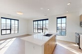 Located at 1875 29th St in Denver's dynamic RiNo corridor, this thoughtfully designed three-bedroom, two-bathroom residence offers a clean, contemporary aesthetic throughout its single-floor layout. The open-concept living and kitchen area serves as the heart of the home, anchored by a sleek island with a white quartz countertop, an undermount sink, and warm wood cabinetry. Bold black-framed grid windows line the living space, flooding the interior with abundant natural light and framing sweeping views of the Denver skyline and surrounding urban landscape. Light-toned hardwood-style flooring flows throughout the main living areas, complementing the crisp white walls and modern finishes. The primary bedroom features carpet flooring, a ceiling fan, and access to a dedicated walk-in closet outfitted with wire shelving for organized storage. The two bathrooms are finished with wood-toned floating vanities, white quartz countertops, and tile work — one featuring a glass-enclosed walk-in shower with white subway tile and a built-in shelf. Additional bedrooms offer carpet flooring, generous natural light, and city views through large black-framed windows. A stacked washer and dryer unit is conveniently housed within the residence, completing this well-appointed urban home.