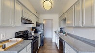 This single-floor residence offers a thoughtfully designed layout that balances functionality and comfort throughout its key living areas. The galley-style kitchen is efficiently organized with white cabinetry lining both sides, granite-look countertops, dark hardwood-style flooring, and a full suite of black appliances including an electric range, refrigerator, and dishwasher. An overhead range hood and flush-mount ceiling light complete the space. The open living room features the same durable hardwood-style flooring, neutral white walls, and a textured ceiling, creating a bright and versatile area. Adjacent to the living room, the dining area benefits from large sliding glass doors that invite abundant natural light and provide a direct view of the landscaped outdoor surroundings. The bedrooms are finished with warm neutral carpet and feature natural light from windows with blinds; one bedroom includes a ceiling fan and another offers a louvered closet door for added storage. The bathroom is clean and well-appointed, featuring a full tub-shower combination, a vanity with granite-look countertop, wood-style flooring, and crisp white finishes throughout. The overall ambiance of the space is clean, bright, and move-in ready.