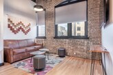 Located at 317 E Wilson St in Madison, WI, this one-bedroom, one-bathroom space blends industrial character with contemporary design across a single thoughtfully laid-out floor. Soaring ceilings with exposed wooden beams and warm wood accents lend a loft-like aesthetic throughout.

The kitchen is a standout feature, offering dark shaker-style cabinetry, light quartz countertops, a classic subway tile backsplash, and a full suite of stainless steel appliances including a range, refrigerator, dishwasher, and microwave. Open floating shelves add functional display space, while a central island with pendant lighting provides additional prep and seating area.

The bedroom is a cozy, well-proportioned retreat with warm earth-toned walls, high ceilings with exposed beam details, light hardwood flooring, a built-in closet, and a wall-mounted television. A hallway connecting the rooms features exposed brick, continuing the industrial aesthetic and leading to a dedicated workspace alcove.

The bathroom is finished with large-format dark marble-style tile flooring, a glass-enclosed walk-in shower, a wood-toned vanity with a white countertop, and a large mirror. Clean white walls keep the space feeling bright and fresh. Throughout, the design achieves a cohesive balance of raw architectural elements and modern, polished finishes.