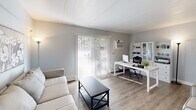 Located at 321 Harbor Dr in Claymont, Delaware, this efficiently designed single-floor residence offers one bedroom, two bathrooms, a dedicated office, and a well-appointed layout across a comfortable footprint. The living room provides a welcoming entry point, featuring light wood-style flooring, neutral gray walls, and a sliding glass door fitted with vertical blinds that allow ample natural light. Adjacent to the living area, the office space — also accessible via a sliding glass door — offers a bright, functional workspace with generous natural light. A separate office room with carpet flooring, closet storage, and a window with bold accent curtains provides additional flexible space. The dining area is defined by a pendant light fixture and soft gray walls accented with decorative framed mirrors, creating an intimate yet open atmosphere. The kitchen is well-equipped with white shaker cabinetry, granite-look countertops, stainless steel appliances including a refrigerator and dishwasher, and wood-style flooring that flows seamlessly into the dining space. The primary bedroom features a striking teal accent wall, carpeted flooring, and a private en-suite bathroom, offering a comfortable retreat. Both bathrooms are clean and functional, featuring white vanities and ample storage. A hallway connects the rooms efficiently throughout the home.