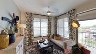 This single-floor residence offers a thoughtfully designed layout with modern finishes throughout. The living area serves as the heart of the home, featuring light wood-style flooring, a ceiling fan, and corner placement of two large windows dressed with bold ikat-patterned curtains, allowing natural light and outdoor views to fill the space.

The kitchen is a standout feature, showcasing dark espresso cabinetry that reaches ceiling height, granite countertops, a subway tile backsplash with under-cabinet lighting, stainless steel appliances, and a central island with seating for multiple guests. Track lighting illuminates the workspace effectively.

The bedrooms are carpeted and well-sized, each equipped with ceiling fans and windows with outdoor views. Decorative curtain panels add character to each room. The primary bedroom connects to a private bathroom featuring a granite-topped vanity, a glass-enclosed walk-in shower, and direct access to a spacious walk-in closet. A second bathroom offers a soaking tub and shower combo, granite vanity, and its own walk-in closet access. The overall aesthetic balances contemporary design with warm, residential comfort.