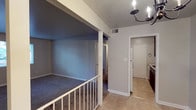 This single-floor residential unit offers a functional and well-organized layout across a series of interconnected rooms. The living area is defined by soft carpeting and a distinctive split-level design, with a white railed divider separating the stepped sections of the space. An elegant chandelier adds a decorative touch overhead, while a large window in the front room allows natural light to filter in with views of the surrounding exterior.

The galley-style kitchen is efficiently designed with rich dark wood cabinetry lining both walls, light-colored countertops, a coil-burner electric range, a dishwasher, and a stainless steel sink. Tile flooring runs throughout the kitchen, complementing the cabinetry's warm tones.

The unit includes multiple bedrooms, each finished with plush wall-to-wall carpeting and neutral-toned walls. The primary bedroom features access to a full bathroom and a dedicated closet, while additional bedrooms offer windows with blinds and ample floor space. The bathroom is appointed with a wall-mounted sink, a lighted medicine cabinet, and chrome fixtures, maintaining a clean and practical aesthetic throughout. Overall, the space presents a straightforward, move-in-ready layout suitable for everyday residential living.