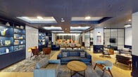 Located at 484 Spadina Avenue in Toronto's vibrant Harbord Village neighbourhood, this thoughtfully designed single-floor amenity space offers a refined and multifunctional environment. The interior is anchored by a rich navy blue and warm wood colour palette, with coffered ceilings, recessed lighting, and herringbone-patterned hardwood flooring that together establish a polished, contemporary ambiance throughout.

The expansive main lounge is furnished with an eclectic mix of blue sofas, mid-century armchairs, and layered area rugs, creating a welcoming atmosphere suited for both relaxation and socializing. Built-in navy shelving units with curated décor accents and a sleek fireplace add character and warmth to the space. A dedicated screening room features tiered bench seating adorned with colourful cushions, a ceiling-mounted projector, and acoustic wall paneling for an immersive viewing experience.

A formal meeting area includes a large boardroom-style table with ample seating, while glass-partitioned zones provide semi-private spaces for focused work or smaller gatherings. A mounted flat-screen television and additional lounge seating complete a more intimate sitting area. The space connects to a larger mixed-use building lobby with soaring ceilings, exposed industrial ductwork, and expansive glazing that floods common areas with natural light.