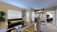This thoughtfully designed one-bedroom, one-bathroom residence offers a comfortable and efficient single-floor layout. The living room serves as the heart of the home, featuring crown molding, recessed lighting, and large windows with blinds that invite natural light. The space accommodates both a seating area and a dedicated dining nook with a glass-top table, creating a seamless flow between living and dining. The kitchen is outfitted with light wood cabinetry, granite-style countertops, black appliances including a range, microwave, refrigerator, and dishwasher, and rich hardwood-style flooring that adds warmth and contrast. A set of bifold doors provides additional storage nearby. The bedroom is a generously proportioned retreat featuring vaulted ceilings with a ceiling fan, warm neutral tones, and a walk-in closet with built-in shelving. Large windows allow ample natural light to fill the room. The bathroom includes a single-sink vanity with wood cabinetry, granite-style countertops, a large mirror, and hardwood-style flooring. Throughout the residence, a cohesive neutral palette with warm beige walls and contemporary finishes creates a clean, inviting ambiance.