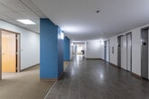 Located at 215 W Pershing Rd in Kansas City, Missouri, this single-floor commercial office space offers a well-organized and functional layout suited for a range of professional uses. The floor plan reveals an expansive arrangement of private offices, open work areas, and common spaces connected by a wide, tiled corridor accented with teal-blue wall panels and wall-mounted lighting, creating a clean and navigable pathway throughout.

Private offices are carpeted with neutral tones and feature drop-panel ceilings with recessed fluorescent lighting. Several offices include large windows that frame views of the surrounding Kansas City cityscape, allowing ample natural light to fill the rooms. Some offices come equipped with built-in wood cabinetry and desking, providing practical workspace solutions.

Transitional areas and reception-style spaces incorporate the building's signature teal accent walls paired with light wood trim, lending the suite a cohesive, professional aesthetic. Sidelight windows flanking interior office doors enhance transparency and the sense of openness between spaces.

A kitchenette serves the suite with laminate cabinetry, countertops, a stainless steel sink, and a dishwasher, providing convenient amenities for daily use. Elevator access is available within the building. The overall environment is bright, organized, and move-in ready for a variety of office configurations.