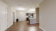 This single-floor residence offers a thoughtfully designed open-concept layout that seamlessly connects the living area and kitchen, creating a bright and cohesive living environment. Rich hardwood-style flooring extends throughout the main living spaces, complemented by warm neutral-toned walls that lend the interior a clean, modern aesthetic.

The kitchen is a standout feature, equipped with dark espresso-stained cabinetry, sleek white countertops, and a full suite of stainless steel appliances including a gas range, microwave, and refrigerator. A peninsula with pendant lighting defines the kitchen's boundary with the living area, while a dedicated dining space is accented by an elegant chandelier overhead. A subway tile backsplash adds a refined finishing touch to the kitchen's design.

The bathroom is well-appointed with a full tub-shower combination, a dark-cabinetry vanity with a white countertop, a large mirror, and hardwood-style flooring that ties it cohesively to the rest of the unit.

The bedroom offers plush carpeting for comfort, a ceiling fan, a bright window that invites natural light, and access to a walk-in closet, providing generous storage. Overall, the space combines functional design with modern finishes for a comfortable and stylish living experience.