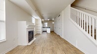 This two-story home offers a clean, neutral aesthetic throughout, with a layout designed to maximize functionality and comfort across both levels. The main floor features an open-concept living and dining area finished with warm wood-look flooring that extends seamlessly toward the kitchen. A tile-surround fireplace serves as a focal point in the living room, flanked by built-in shelving and framed by large windows that allow ample natural light to fill the space. A staircase with white balusters leads to the upper level, adding architectural interest to the main floor.

The kitchen is well-appointed with white cabinetry, dark speckled countertops, a center island, white appliances including a range and dishwasher, and a double sink beneath a window. Multiple doorways provide convenient access to adjacent spaces, including storage areas near the entry.

Upstairs, the bedrooms are carpeted and generously sized, each featuring closets with double doors and windows that bring in natural light. Ceiling heights on the upper level feel notably open. The bathroom includes a full tub-shower combination, a vanity with storage, and wood-look tile flooring, maintaining the home's cohesive, light-toned palette throughout.