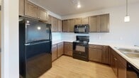 This two-story, 2-bedroom, 2-bathroom home is thoughtfully laid out across two levels, offering a comfortable and functional living environment. The main floor features an open-concept living room and kitchen area, unified by light-toned hardwood-style flooring. The kitchen is well-appointed with rich, warm-toned wood cabinetry, white countertops, and a full suite of black appliances including a refrigerator, electric range, and over-the-range microwave. A breakfast bar adds additional counter space and casual seating. Recessed lighting and pendant fixtures illuminate the area throughout. A staircase with a modern metal railing connects the two floors. The upper level hosts both bedrooms, each carpeted for comfort. The primary bedroom offers a generous footprint with access to a walk-in closet featuring wire shelving for organized storage. The second bedroom is bright, with a large window providing views to the outdoors and light hardwood-style flooring. Two full bathrooms serve the home, each featuring tile flooring, a vanity with dark wood cabinetry, and a tub-shower combination. A dedicated laundry room with a full-size washer and dryer provides added convenience. The space is clean, modern, and move-in ready.