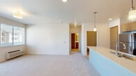 This single-floor residence showcases a clean, contemporary design throughout. The open-concept kitchen serves as a central hub, featuring warm-toned flat-front cabinetry, stainless steel appliances including a refrigerator, range, and built-in microwave, and a generously sized island with a white quartz countertop and undermount sink. Pendant lighting adds a refined touch overhead, while light hardwood-style flooring grounds the space. An in-unit washer is conveniently located just off the kitchen area.

The living areas transition smoothly from hard flooring to plush carpeting, creating distinct zones within the open layout. Bedrooms are well-proportioned, each equipped with ceiling fans and ample natural light. One bedroom offers direct access to a private balcony through a sliding glass door, providing views of the surrounding neighborhood. Both bedrooms feature walk-in closets outfitted with wire shelving systems for versatile storage.

The full bathroom is finished with light wood-grain vanity cabinetry, a white quartz countertop, a large mirror, and a tub-shower combination. Clean white walls and neutral tones carry throughout the entire residence, contributing to a bright, cohesive, and move-in-ready ambiance.