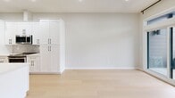 Located at 9 John St in Clinton, CT, this thoughtfully designed two-bedroom, one-bathroom home offers a clean, modern aesthetic with high-quality finishes throughout. Light-toned hardwood flooring runs seamlessly across the single-floor layout, creating a bright and cohesive feel.

The kitchen serves as the centerpiece of the home, featuring a large waterfall quartz island with an undermount sink and matte black faucet, white shaker cabinetry with black hardware, stainless steel appliances, and subway tile backsplash. Pendant lighting with black-and-gold fixtures adds a contemporary touch, while a sliding barn door nearby provides a stylish architectural accent.

The spacious primary bedroom receives generous natural light through a large window with outdoor views of mature trees and the surrounding neighborhood. The second bedroom includes a walk-in closet with built-in shelving, offering practical storage.

The bathroom is well-appointed with a white shaker vanity, undermount sink, matte black fixtures, a frameless glass sliding shower enclosure with a soaking tub, and neutral tile flooring and walls. Recessed lighting and a modern vanity light complete the polished look.

Throughout the home, neutral wall tones, recessed lighting, and clean white trim contribute to a bright, move-in-ready atmosphere suited for comfortable everyday living.