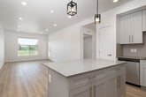 This well-designed 2-bedroom, 2-bathroom unit in Idaho Falls, Idaho offers a clean, modern aesthetic throughout its efficiently laid-out single floor. The open-concept kitchen and living area serves as the heart of the space, anchored by a generously sized island with quartz countertops and pendant lighting above. The kitchen is outfitted with crisp white shaker cabinetry, subway tile backsplash, brushed gold hardware, and a full suite of stainless steel appliances including a refrigerator, range, microwave, and dishwasher. Light wood-style flooring runs throughout the main living areas, complementing the bright white walls and recessed lighting that keep the space feeling open and airy. The living room receives natural light through a large window with outdoor views of the surrounding greenery. The primary bedroom features a tray ceiling with recessed lighting, plush carpet, a window with balcony access, and an en-suite bathroom complete with a granite-topped vanity, undermount sink, and a soaking tub with shower. The second bedroom is equally bright with soft carpet flooring. The second bathroom mirrors the same refined finishes, including a tub-shower combination and matching vanity. Two hallways connect the space efficiently, adding to the overall functional flow of the layout.