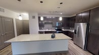 This single-floor residence at 3655 Prairie Waters in Grand Prairie, Texas, offers a well-designed layout with modern finishes and a cohesive contemporary aesthetic. The open-concept kitchen serves as the centerpiece of the living area, showcasing dark espresso cabinetry, a gray subway tile backsplash, stainless steel appliances — including a refrigerator, range, microwave, and dishwasher — and a generous granite-topped island ideal for meal prep or casual dining. Pendant lighting and a track light system illuminate the space, while wood-look plank flooring adds warmth and continuity throughout the main areas. The entryway features a solid, paneled front door and easy access to a closet, providing a clean and functional arrival experience. The bedrooms are carpeted for comfort, each equipped with a ceiling fan and light fixture, and feature window blinds that allow for natural light and privacy. One bedroom benefits from dual windows, enhancing its brightness. The bathrooms are finished with granite vanity countertops, dark cabinetry, and light wood-look tile flooring. One bathroom includes a tub-shower combination with tile surround, while another offers a glass-enclosed shower. Both bathrooms provide direct access to well-organized walk-in closets with built-in shelving systems.
