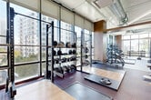 Located at 125 NE 32nd St in Miami's vibrant Upper Eastside neighborhood, this generously sized fitness center delivers a comprehensive, professional-grade workout environment across a single open floor. The space is defined by its dramatic floor-to-ceiling windows that wrap around multiple sides of the room, flooding the interior with abundant natural light and offering sweeping views of the surrounding Miami skyline and cityscape.

The layout is thoughtfully organized into distinct functional zones. A dedicated strength training area features power racks, barbell stations, and a full dumbbell rack, complemented by rubber flooring and lifting platforms designed for heavy use. An extensive selection of selectorized cable machines and resistance equipment anchors the central zone, while a cardio section lines the window-facing wall with a row of treadmills and other aerobic machines positioned to take full advantage of the outdoor views.

Additional amenities include full-length wall mirrors that enhance the sense of openness, built-in storage lockers, and an exposed industrial-style ceiling with polished ductwork that adds an urban, modern aesthetic. Warm wood accent columns contrast with the cool gray tones of the walls, creating a balanced and motivating atmosphere. The facility is well-equipped for a wide range of fitness needs, from functional training to traditional strength and conditioning.