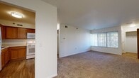 Located at 1713 Cresthill Ave in Royal Oak, Michigan, this single-floor unit offers a clean, functional layout with a straightforward design throughout. The kitchen is equipped with warm oak cabinetry extending to the upper walls, white laminate countertops in an L-shaped configuration, a white electric range with coil burners, an over-the-range microwave, and a stainless steel sink — providing ample storage and prep space in a compact, efficient arrangement. The kitchen transitions openly into the living area, which features neutral carpet flooring, bright white walls, and a large window dressed with vertical blinds that allows generous natural light to fill the room. The open-plan design creates a sense of spaciousness between the living and kitchen zones. The bedrooms are carpeted and well-lit by windows overlooking the surrounding greenery, offering a quiet, comfortable setting. One bedroom features access to a walk-in closet, adding notable storage capacity. The bathroom is finished with white square tile surrounding a full soaking tub and shower, a wood-toned vanity with a light countertop, and wood-look vinyl plank flooring, giving it a clean and practical finish. The overall aesthetic is neutral and move-in ready.