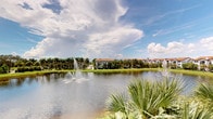 This single-story property is situated within a beautifully landscaped community that evokes the charm of a classic Florida setting. The standout feature of the surrounding environment is a tranquil community lake, graced with elegant tiered water fountains that add both visual interest and a soothing ambiance to the outdoor scenery. Lush, manicured lawns extend along the water's edge, framed by an abundance of tall palm trees that lend the setting a distinctly tropical character. Residential buildings nearby display warm terracotta rooflines and Mediterranean-inspired architecture, contributing to the cohesive and inviting aesthetic of the community. The wide-open sky above, with its dynamic cloud formations, enhances the sense of openness and natural beauty. The property benefits from its proximity to these well-maintained common grounds, offering a peaceful and picturesque outdoor environment. The combination of waterfront views, lush greenery, and thoughtful landscaping creates a serene atmosphere that is characteristic of sought-after communities in warm, sun-drenched climates. Interior images were not sufficiently illuminated to provide detailed room descriptions; however, the overall setting strongly suggests a comfortable and well-appointed single-floor living space within this vibrant, resort-style community.