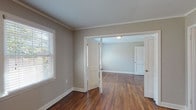 This single-story, two-bedroom, one-bathroom residence offers a cohesive and practical layout accentuated by rich, dark hardwood floors that run throughout the living areas and bedrooms. Crown molding adds a classic architectural detail to each room, lending a polished, finished look to the neutral gray walls and crisp white trim.

The living and dining areas connect fluidly, with natural light filtering through white-slatted blinds on multiple windows. French-style interior doors between rooms enhance the open feel while maintaining defined spaces. An entry area provides a natural transition point into the rest of the home, with a glimpse into the kitchen beyond.

The kitchen is efficiently designed, featuring warm wood cabinetry, stone-patterned countertops, and black appliances including a gas range and dishwasher. A window above the sink brings in additional natural light.

Both bedrooms are generously proportioned, each featuring hardwood floors, crown molding, and ample natural light from multiple windows. Each bedroom includes a closet with a hanging rod for convenient storage.

The bathroom is clean and classic, with white subway-style wall tile surrounding a tub/shower combination, a pedestal sink, and a window that provides natural ventilation and light.