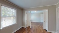 This single-story, two-bedroom, one-bathroom residence offers a cohesive and practical layout accentuated by rich, dark hardwood floors that run throughout the living areas and bedrooms. Crown molding adds a classic architectural detail to each room, lending a polished, finished look to the neutral gray walls and crisp white trim.

The living and dining areas connect fluidly, with natural light filtering through white-slatted blinds on multiple windows. French-style interior doors between rooms enhance the open feel while maintaining defined spaces. An entry area provides a natural transition point into the rest of the home, with a glimpse into the kitchen beyond.

The kitchen is efficiently designed, featuring warm wood cabinetry, stone-patterned countertops, and black appliances including a gas range and dishwasher. A window above the sink brings in additional natural light.

Both bedrooms are generously proportioned, each featuring hardwood floors, crown molding, and ample natural light from multiple windows. Each bedroom includes a closet with a hanging rod for convenient storage.

The bathroom is clean and classic, with white subway-style wall tile surrounding a tub/shower combination, a pedestal sink, and a window that provides natural ventilation and light.