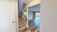 Located at 2951 Tachevah Dr in Santa Rosa, CA, this efficiently designed single-floor space offers a functional and comfortable layout comprising an entrance, a living room, and a bathroom. The interior is finished with durable wood-look laminate flooring that runs consistently throughout, lending a cohesive and modern aesthetic to the entire space.

The entrance greets visitors with a carpeted staircase featuring a sleek black metal railing, providing access to upper levels. Adjacent to the entryway, the living room is a bright and open area bathed in natural light, courtesy of multiple windows and a sliding glass door that opens to an outdoor view of lush greenery. Warm beige walls complement the light tones of the flooring, while a ceiling fan adds both function and a casual finishing touch. The textured ceiling is a consistent detail found throughout the space.

The kitchen area, visible in the dollhouse view, is neatly positioned alongside the living space and includes standard appliances and a white cabinetry setup. The bathroom is clean and practical, featuring a wide vanity with an undermount sink, a large mirror, wood-look flooring matching the rest of the unit, and a bright window for natural ventilation. Overall, the space presents a bright, neutral, and move-in-ready environment.