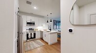 This thoughtfully designed one-bedroom, one-bathroom residence offers an efficient and stylish layout across a single floor. The open-concept kitchen and living area serves as the heart of the home, where crisp white shaker cabinetry, a classic subway tile backsplash, and stainless steel appliances create a clean, contemporary kitchen. A peninsula with bar seating and sleek pendant lighting above adds both functionality and visual appeal, seamlessly connecting the kitchen to the living space. Warm wood-tone flooring flows throughout, anchoring the bright, neutral palette.

The living area is inviting and well-lit, with natural light streaming in through windows fitted with blinds, and access to an exterior door. The bedroom offers a comfortable retreat with multiple windows, ample natural light, and room for generous furnishings. A dedicated closet provides practical storage, while the entrance area transitions smoothly into the main living spaces.

The bathroom is finished with a dual-sink vanity featuring white cabinetry and matte black hardware, a large mirror with lighted surround, and a full tub with marble-style tile surround — delivering a clean, spa-like aesthetic. Smart home features, including a programmable thermostat, add a modern touch throughout this well-appointed residence.