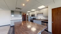 Located at 111 N Fourth St in the heart of downtown Columbus, Ohio, this single-floor commercial space offers a functional and polished layout suited for office or professional use. The standout feature is a generously sized kitchen area, designed with both utility and aesthetics in mind. Gray-toned cabinetry extends across the full perimeter of the kitchen, providing abundant storage with glass-front upper display cabinets adding a refined touch. A large central island anchors the space, topped with a striking marble-veined stone countertop that extends to the perimeter surfaces as well. The kitchen is fully equipped with stainless steel appliances, including a refrigerator, electric range, microwave, dishwasher, and a deep double sink. A drop ceiling with recessed lighting and flush panel light fixtures provides consistent, even illumination throughout the kitchen. Additional rooms within the space include private areas with blinds-covered windows allowing controlled natural light. These rooms appear well-suited for private offices or meeting areas. The overall interior presents a clean, neutral palette with a professional ambiance appropriate for a commercial or office-based environment in a prime downtown Columbus location.