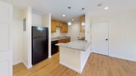 This single-floor, 2-bedroom, 1-bathroom residence offers a clean and functional layout with consistent hardwood-style flooring connecting every room. The kitchen serves as a standout feature, boasting granite countertops, warm wood cabinetry with sleek hardware, and black appliances including a refrigerator, electric range, built-in microwave, and dishwasher. A peninsula island with pendant lighting above provides additional prep space and casual seating, while recessed lighting enhances the overall brightness of the kitchen area. An in-unit washer is also present, adding everyday convenience. Both bedrooms are well-sized, bright, and finished with the same hardwood-style flooring and neutral wall tones. One bedroom features a closet and receives generous natural light through multiple windows, offering pleasant outdoor views. The full bathroom is finished with large-format tile surrounds in the tub/shower combination, complemented by tile flooring, a granite-topped vanity, and classic fixtures. Throughout the residence, white trim and neutral walls create a fresh, cohesive aesthetic. The open flow between the living areas and kitchen makes the space feel welcoming and practical for everyday living.