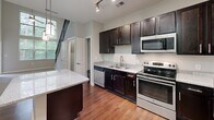 Located at 110 Talisman Way in Raleigh, NC, this two-story residence offers a well-designed layout spread across two floors. The main level is the larger of the two, housing a striking open-concept kitchen equipped with dark espresso cabinetry, granite countertops, stainless steel appliances, a center island, and rich hardwood flooring. Track lighting and pendant fixtures illuminate the space, while large windows allow natural light to pour in with views of surrounding greenery. A dramatic staircase with sleek black metal railings serves as a standout architectural element, connecting both levels with style. The upper floor features the private bedroom, a comfortable and carpeted retreat with a ceiling fan and a window overlooking the wooded surroundings. A dedicated closet and hallway provide practical storage and circulation. The full bathroom is finished with dark wood cabinetry, a white countertop vanity, a tub-shower combination, and wood-look flooring, creating a clean and functional space. Neutral gray tones throughout the home lend a modern, cohesive aesthetic, while the two-story design with soaring ceilings in the stairwell adds a sense of openness and volume to the overall living experience.