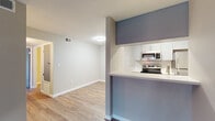This single-floor residence offers a clean, modern aesthetic with consistent design choices carried throughout. The open-concept layout connects the kitchen and living area seamlessly, creating a bright and functional shared space. Light wood-tone flooring runs through the kitchen and dining areas, while richer, darker hardwood-style flooring anchors the living room and bedrooms, adding warmth and contrast.

The galley-style kitchen is well-equipped with stainless steel appliances—including a range, over-the-range microwave, refrigerator, and dishwasher—complemented by grey shaker-style cabinetry, white quartz countertops, and a classic subway tile backsplash. A peninsula with a raised bar extends into the adjacent living space, enhancing the open flow.

The spacious living room features a sliding glass door that opens to an outdoor balcony, allowing for natural light and outdoor access. The bedrooms are generously sized, each with hardwood-style flooring, neutral wall tones, and windows with blinds that bring in natural light.

The bathroom includes a grey vanity with white countertop, a large mirror with overhead lighting, and a tub-shower combination with tiled surround. A stylish barn door adds a contemporary touch to the bathroom entry, rounding out the modern, cohesive design of this comfortable residence.