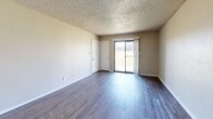 This single-floor unit offers a practical and straightforward layout with a variety of flooring and finish options across its main spaces. The living area is a generously sized room finished with wood-look laminate flooring and a textured popcorn ceiling. A sliding glass door fills the space with natural light and provides direct outdoor access, while a standard interior door offers additional entry points within the layout.

The galley-style kitchen runs parallel walls lined with warm-toned wooden cabinetry, both upper and lower, offering substantial storage throughout. Light-toned laminate countertops complement the cabinetry, and the kitchen is equipped with a white electric range, dishwasher, and refrigerator. Wood-look flooring extends through this space, and an overhead light fixture provides functional illumination.

The bedrooms feature neutral carpet flooring and textured walls finished in light beige tones. White trim and baseboards frame each room cleanly. One bedroom includes a window with blinds that allows natural light to enter. Additional rooms in the unit continue the consistent use of neutral wall colors, carpet, and white-trimmed doors with brass hardware, contributing to a cohesive and understated aesthetic throughout the space.
