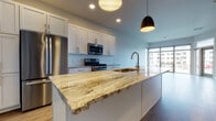 Located at 3600 S Point Rd in Verona, Wisconsin, this single-floor residence combines contemporary design with thoughtful functionality throughout its well-appointed layout. The open-concept kitchen serves as a centerpiece, showcasing a large island topped with richly veined natural granite that extends generously for both meal prep and casual dining. White shaker-style cabinetry lines the walls, complemented by a classic subway tile backsplash and a full suite of stainless steel appliances, including a gas range, built-in microwave, and French door refrigerator. Pendant lighting adds a refined touch above the island. The adjacent living area is bright and expansive, featuring wide-plank hardwood-style flooring and floor-to-ceiling windows with a glass door leading to a private balcony, flooding the space with natural light and outdoor views. Bedrooms are carpeted for comfort, with one featuring a generously sized walk-in closet with built-in shelving. The bathroom includes white cabinetry, granite countertops, and warm wood-tone flooring. Throughout the unit, neutral tones, clean lines, and quality finishes create a cohesive, modern ambiance.