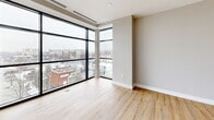 Located on Farmington Avenue in West Hartford, CT, this contemporary one-bedroom, one-bathroom unit offers a well-designed layout with modern finishes throughout. The open-concept living and kitchen area is anchored by striking floor-to-ceiling black-framed windows that flood the space with natural light and offer expansive views of the surrounding West Hartford streetscape. Light-toned hardwood-style flooring runs throughout the main living areas, enhancing the bright and airy atmosphere.

The kitchen is thoughtfully appointed with dark shaker-style cabinetry, stainless steel appliances including a refrigerator, range, and microwave, a white tile backsplash, and a peninsula with a light countertop and matte black pendant lighting overhead — ideal for both cooking and casual dining.

The bedroom features plush carpeting, a dual-door closet, and a window with a view, complemented by a soothing two-tone color palette of soft blue and warm taupe. The full bathroom includes large-format tile flooring and clean, minimal finishes. A dedicated laundry area with side-by-side washer and dryer, wood-look flooring, and built-in shelving adds everyday convenience. This unit combines urban energy with refined residential comfort.