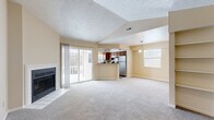 This single-floor residence offers a practical and comfortable layout across three bedrooms and two bathrooms. The living room serves as the heart of the home, featuring a striking vaulted ceiling, a cozy fireplace, and sliding glass doors that open to an outdoor balcony, filling the space with natural light. Built-in shelving adds functional character to one wall, while plush carpeting runs throughout the living and bedroom areas. The open-concept kitchen overlooks the living room via a peninsula counter, and is equipped with warm wood cabinetry, laminate countertops, stainless steel appliances including a refrigerator and dishwasher, and windows that bring in additional natural light. Wood-look flooring ties the kitchen together seamlessly. The primary bedroom offers generous proportions with ample closet space featuring sliding doors. The two additional bedrooms are bright and well-sized, each with carpet flooring and neutral walls. Both bathrooms are finished with wood-toned cabinetry and light countertops; one includes a tub-shower combo, while the other features a walk-in glass shower. A hallway connects the private areas of the home, and a dedicated closet provides additional storage. The overall ambiance is clean, neutral, and move-in ready.