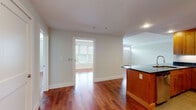 This single-floor residence combines thoughtful design with quality finishes to create a comfortable and functional living space. Rich, polished hardwood floors flow continuously throughout the main living areas, reflecting natural light and lending warmth to every room.

The open-concept layout connects the living area to the kitchen, which is a standout feature of the home. Outfitted with warm wood cabinetry, dark granite countertops, stainless steel appliances including a gas range, microwave, refrigerator, and dishwasher, the kitchen also offers an island peninsula that provides additional prep space and casual seating. Recessed lighting illuminates the workspace efficiently.

The living area is generously proportioned, with large windows fitted with blinds that allow for controlled natural light. A front entry door with sidelights further brightens the space. The bedrooms continue the hardwood flooring theme and feature ample closet storage, including a double-door closet in one room, along with windows that bring in natural greenery views.

The bathroom is finished with elegant marble tile on both the walls and countertop surfaces, paired with a crisp white vanity, chrome fixtures, and a large mirror. The overall palette of soft neutral walls and white trim creates a clean, cohesive aesthetic throughout the residence.